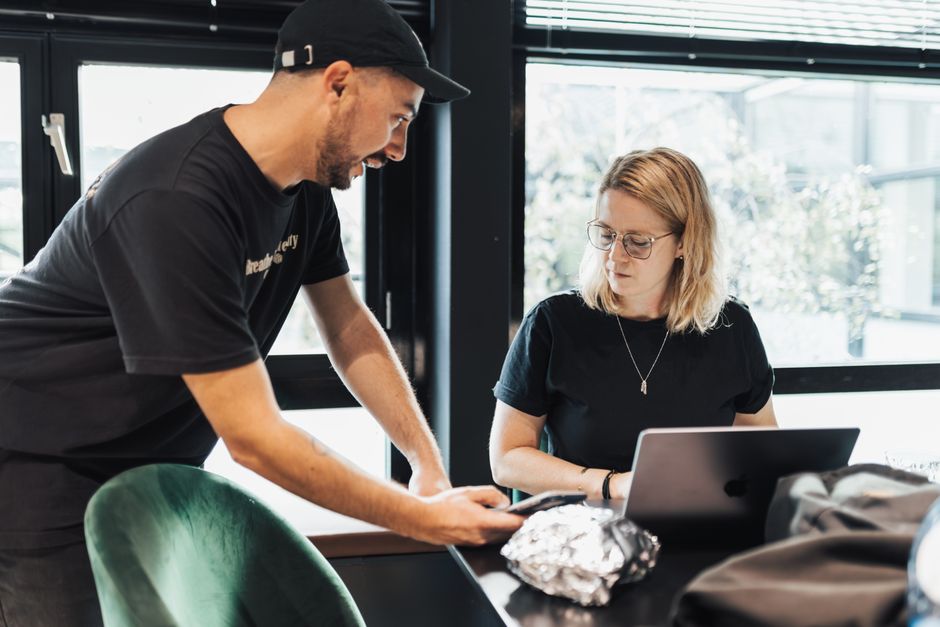 Un homme et une femme collaborent dans un bureau, utilisant un ordinateur portable et un appareil mobile pour des tâches professionnelles.