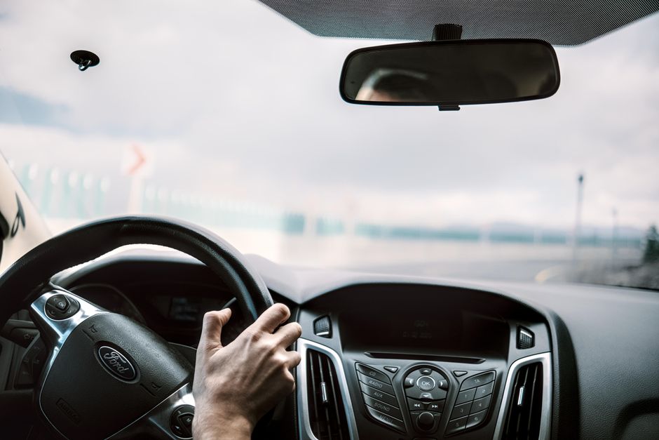 Vue depuis l'intérieur d'une voiture montrant le volant, le rétroviseur et la route floue en arrière-plan.