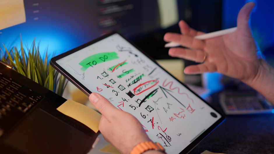 Une personne gère des tâches sur une tablette avec un stylet numérique dans un bureau moderne.
