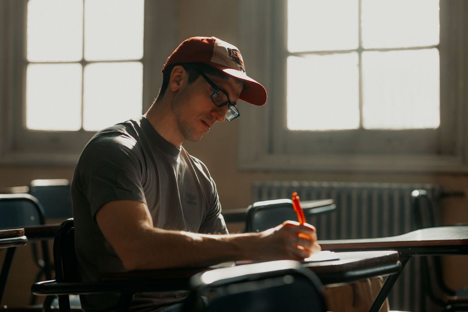 Étudiant dans une salle de classe ensoleillée se concentrant sur ses notes avec un stylo.