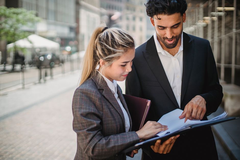 Deux professionnels examinant des documents en extérieur dans un environnement urbain.