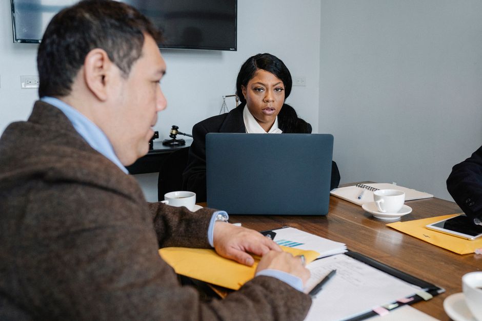 Groupe de collègues multiethniques en tenue formelle assis à une table avec un ordinateur portable et des documents tout en discutant de questions professionnelles.