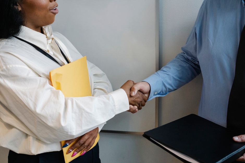 Crop unrecognizable multiethnic colleagues standing with documents and shaking hands while greeting each other in office