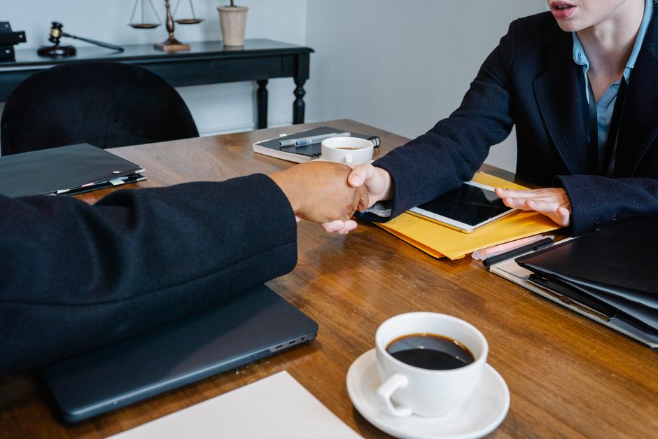 Crop anonymous multiethnic coworkers in elegant outfit shaking hands at table with tablet and documents in office