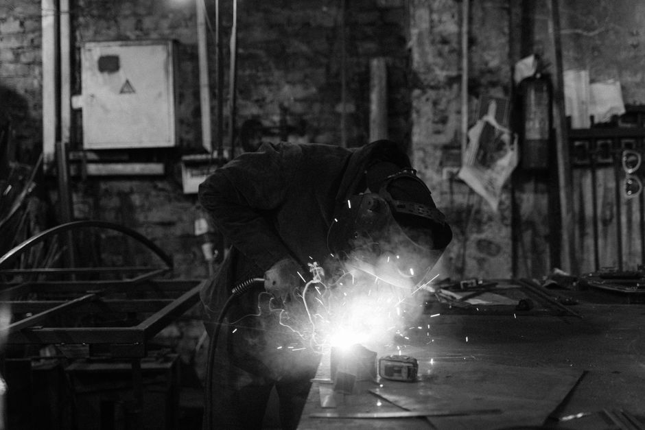 Vue monochrome d'un soudeur effectuant un travail sur métal, des étincelles jaillissant dans un atelier industriel.