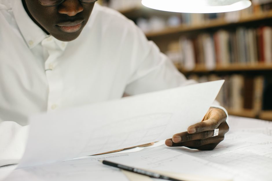 Étudiant analysant des documents dans une bibliothèque sous une lumière vive.