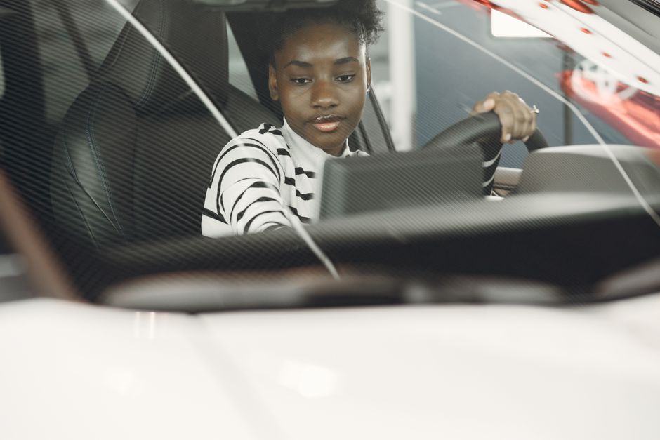 Jeune femme aux cheveux noirs au volant, vue depuis l'intérieur avec une mise au point sur le volant.
