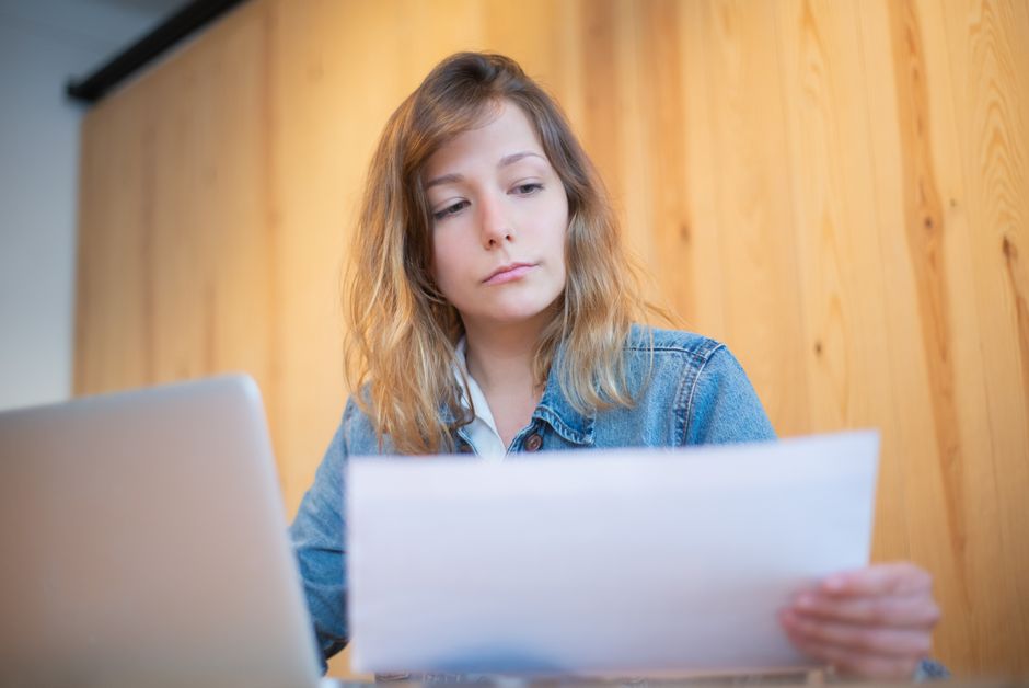 Femme d'affaires en veste en jean analysant des documents sur une table en bois dans un espace de travail chaleureux.