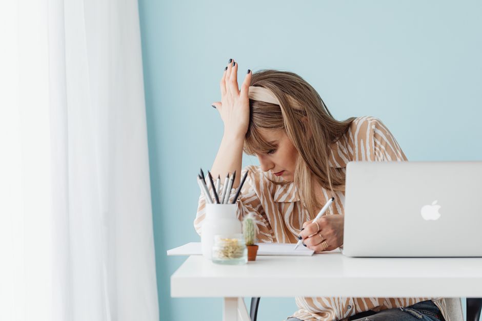 Femme caucasienne la main sur la tête, l'air stressée, travaillant sur un ordinateur portable dans un bureau à domicile.