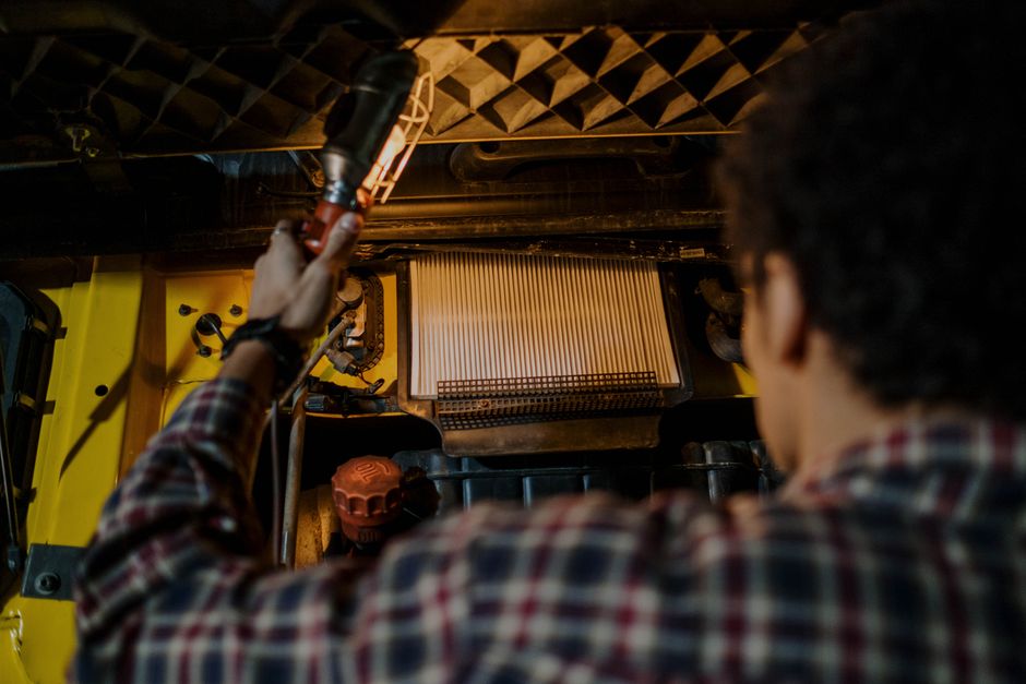 Mécanicien inspectant le moteur d'un véhicule sous le capot avec une lampe portative dans un atelier.