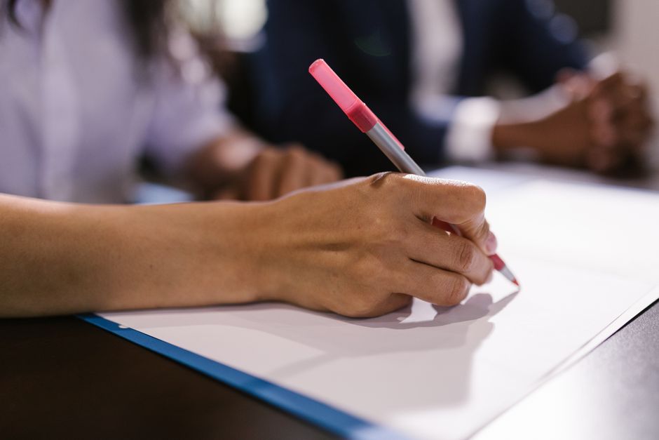 Gros plan détaillé d'une personne écrivant sur du papier avec un stylo dans un bureau.