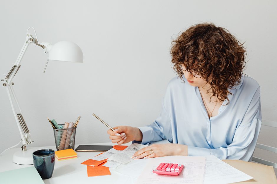 Femme au bureau calculant des dépenses avec des documents, une calculatrice et un café.