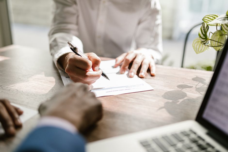 Gros plan sur des personnes signant un document à un bureau, soulignant une interaction professionnelle.