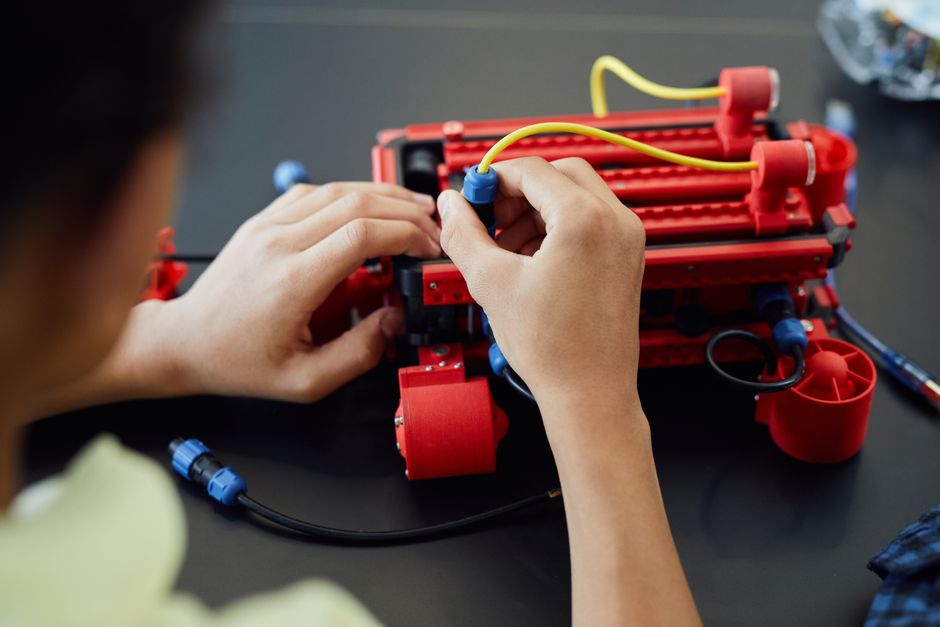 Gros plan sur des mains assemblant un projet robotique avec des câbles en intérieur, illustrant la technologie et l'électronique.