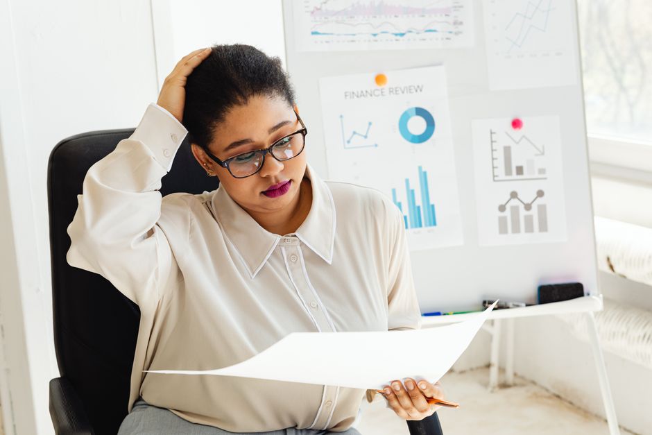 Une femme adulte examine des rapports financiers à son bureau avec des tableaux et des graphiques en arrière-plan.