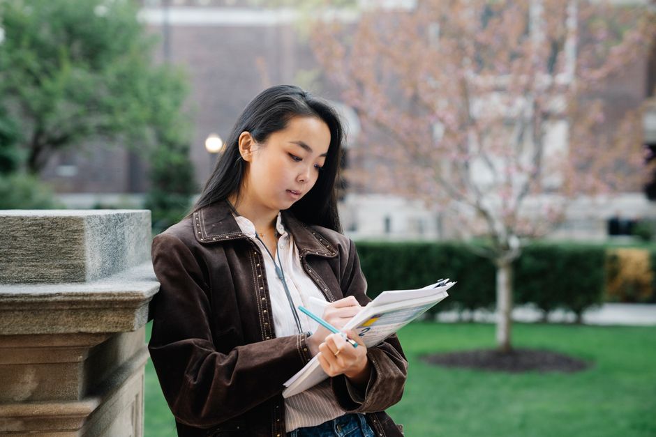 Jeune femme étudiant avec des documents sur un campus universitaire en extérieur.