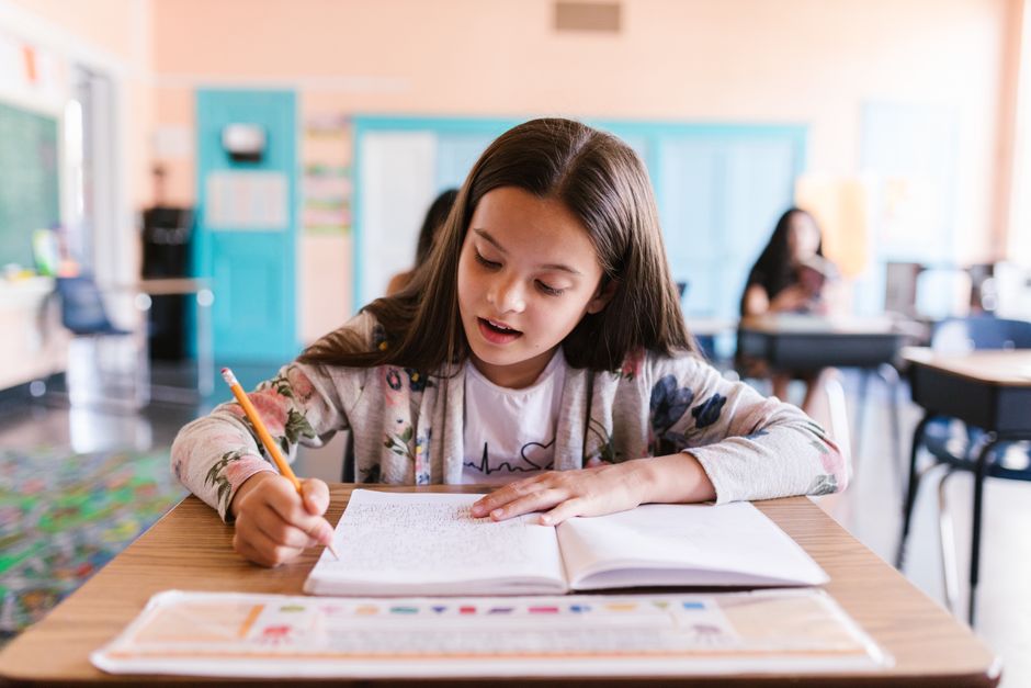 Focused young girl writing in her notebook in a classroom setting, showcasing learning and education.