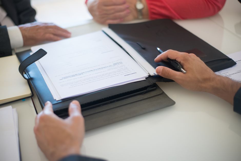 Deux professionnels discutant d'un contrat avec des documents sur une table, en intérieur.