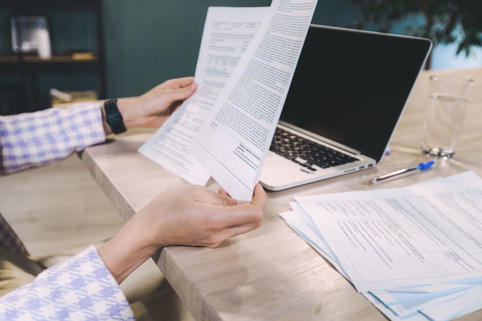 Gros plan sur des mains examinant des documents imprimés à côté d'un ordinateur portable sur un bureau.