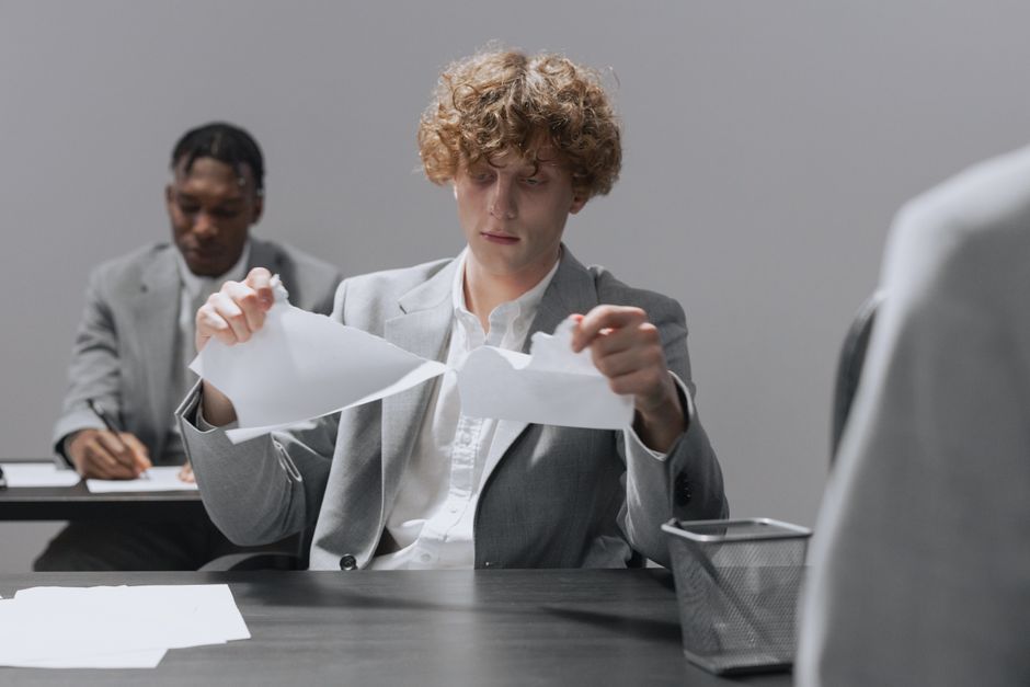 Deux employés en costume assis à des bureaux, dont l'un déchire du papier.